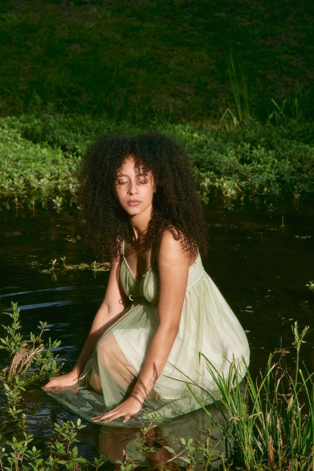 A woman seated in water surrounded by greenery